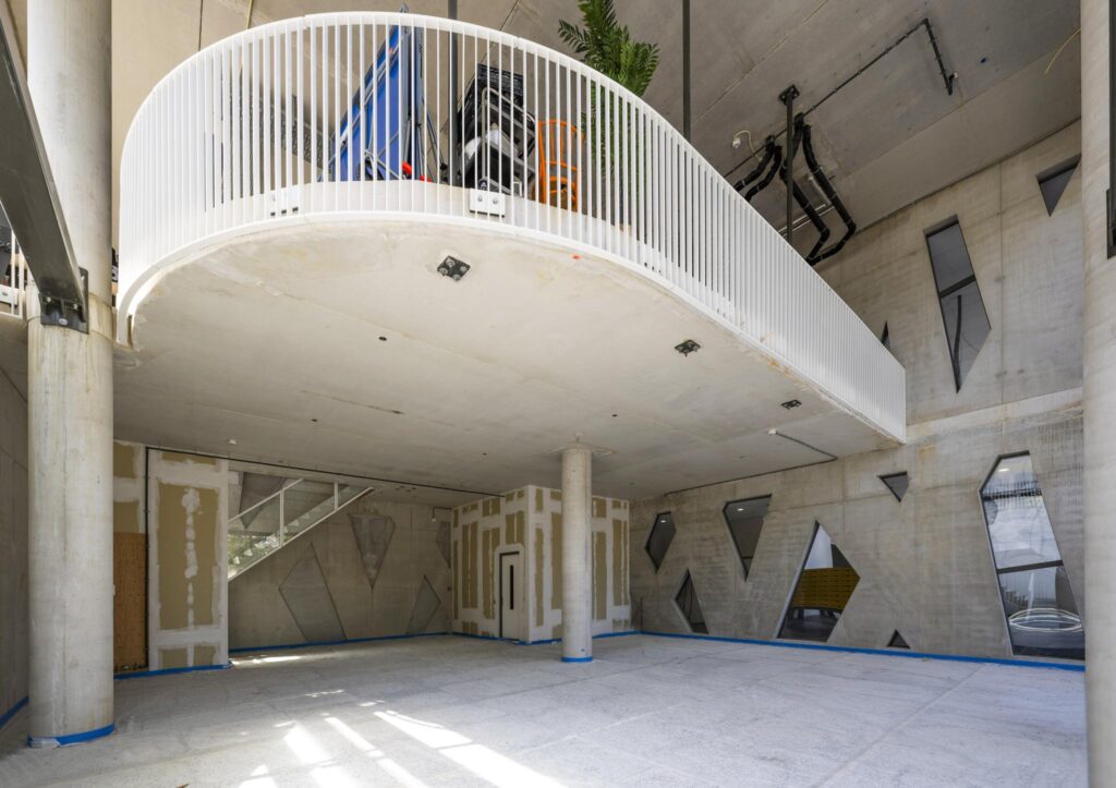 Modern unfinished interior space with concrete walls, angular windows, and a curved mezzanine balcony at Elizabeth Cady Stantonplein.